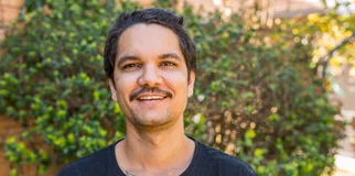 man smiling outside by a bush