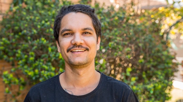 man smiling outside by a bush
