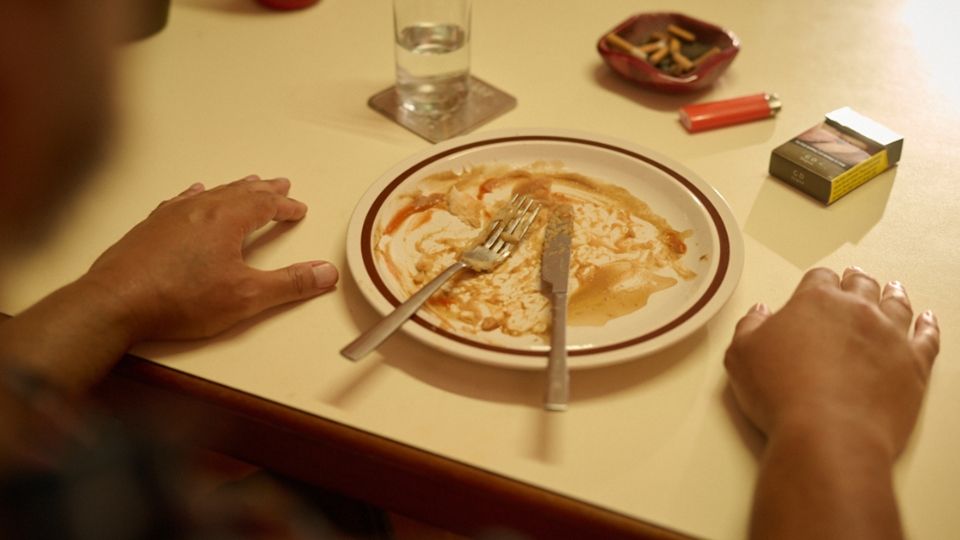 person with an empty plate after dinner and cigarette packet to the side